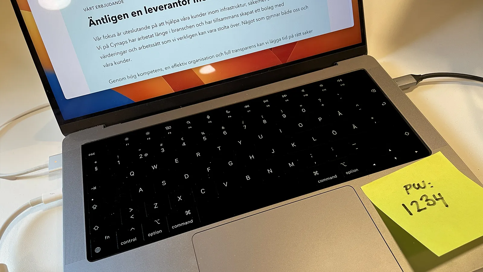 En uppslagen laptop med en post-it fäst på tangentbrädan med texten "PW: 1234".